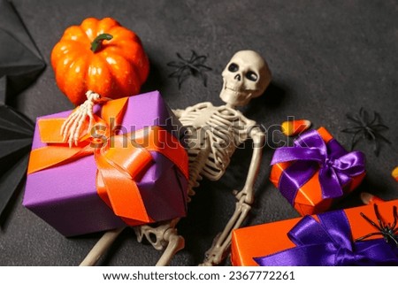 Composition with beautiful gift boxes, skeleton and pumpkin for Halloween on dark background, closeup