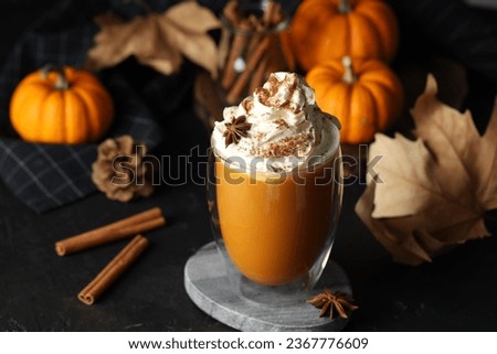 Glass of pumpkin spice latte with whipped cream and ingredients on black table