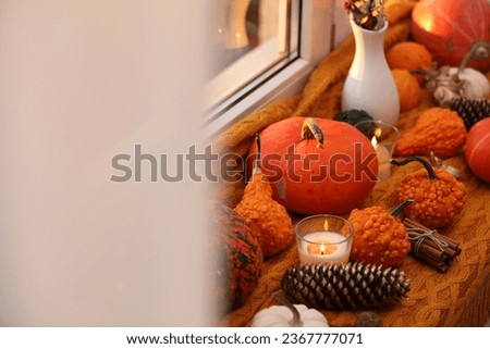 Composition with pumpkins and burning candles on window sill indoors