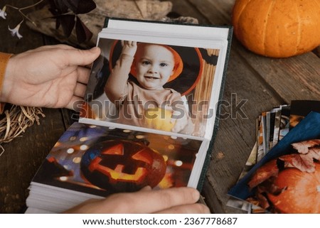 Halloween printed photos. Hands browsing picture album with autumn photos.