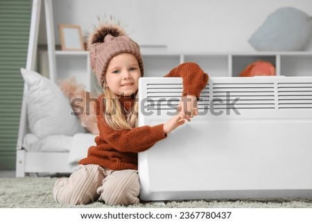 Cute little girl warming near radiator in bedroom Royalty-Free Stock Photo #2367780437