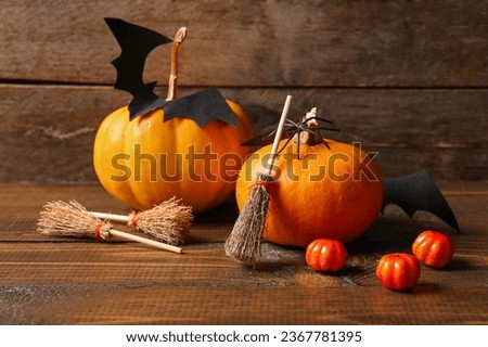 Halloween composition with brooms, pumpkins and bat on brown wooden background