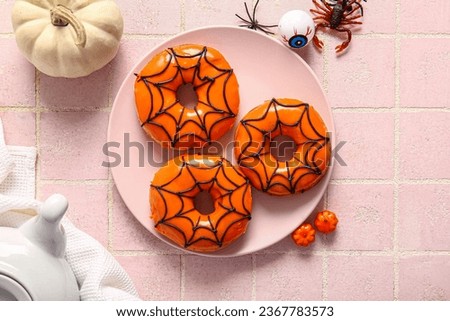 Plate of tasty donuts for Halloween with eye, pumpkin and candies on pink tile background