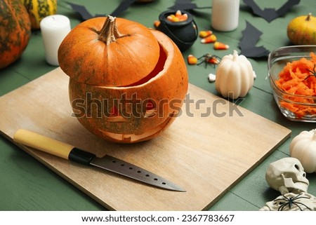 Carved pumpkin with Halloween decorations on green wooden table