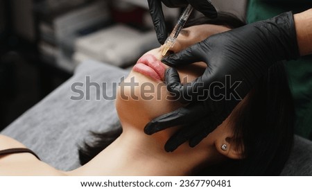 Injection procedure for lip augmentation, close-up. The cosmetologist slowly and carefully injects filler into the client’s lips. Advertising concept for facial care, youth and beauty. Royalty-Free Stock Photo #2367790481