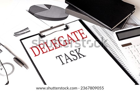 DELEGATE TASK text on a paper clipboard with chart and notebook on withe background
