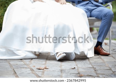 In this intimate shot, we focus on the feet and legs of a newlywed couple as they sit down together. Their shoes and attire symbolize the beginning of a shared journey filled with love, commitment
