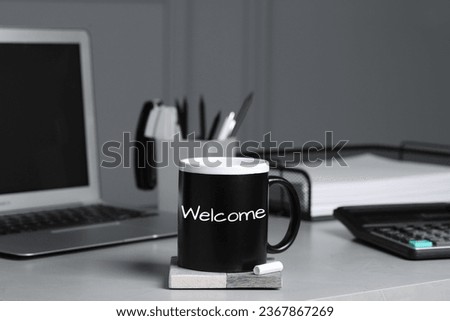 Cup with chalked word Welcome on office desk
