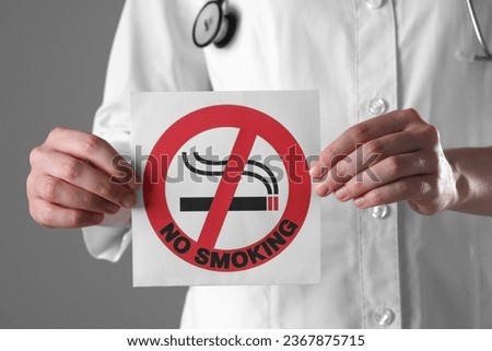 Doctor holding card with no smoking sign on gray background, closeup