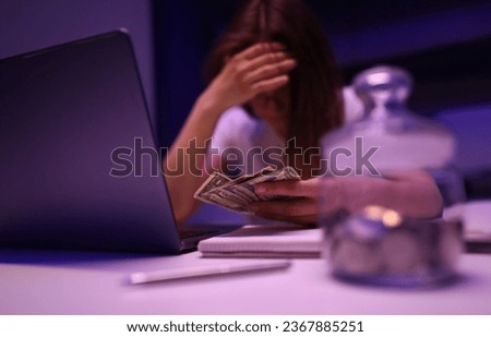 Close-up of depressed woman calculating family financial situation. Person close face with hand and holding banknotes. Glass container with coins. Money and investment concept Royalty-Free Stock Photo #2367885251