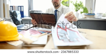 Close-up of creative person in presentable suit working in renovation agency. House plan and palette with colourful sample on wooden table. Interior design and professional architect concept Royalty-Free Stock Photo #2367885333