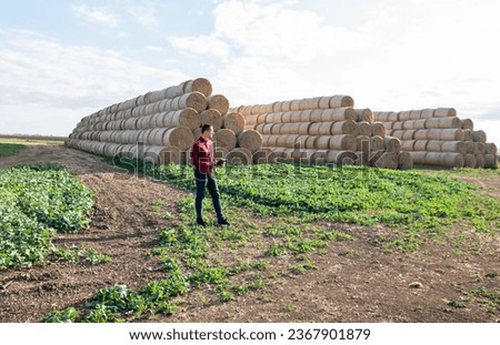 Happy farmer standing near straw hay bales in the field happy with the harvest Royalty-Free Stock Photo #2367901879