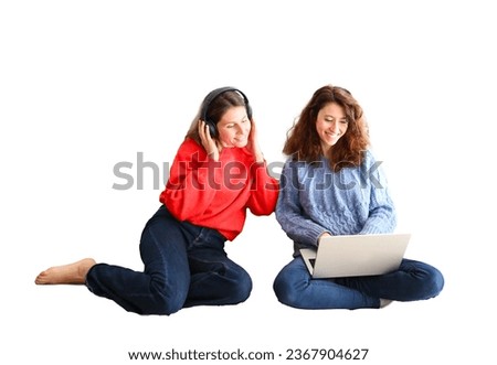 Two female happy friends watching a movie on a laptop computer while wearing headphones against a white background