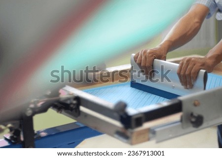 Focus on the work atmosphere of manual screen printing activity with a blurred foreground and background lit by natural light                          