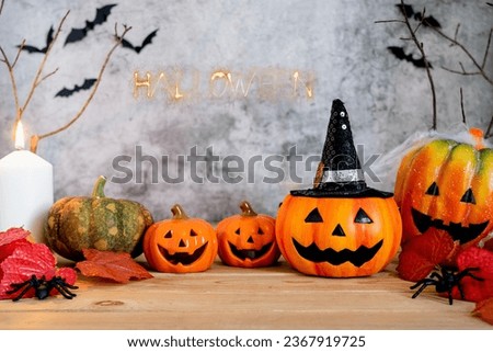Orange pumpkins are laying on the surface of wooden table with cloudy background. The candle, leaves, spiders put there, and bats picture are made in background. All the setup are made for Halloween.