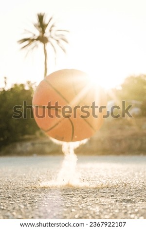 Bright orange ball bouncing on asphalt ground against green trees on sunny day in summer