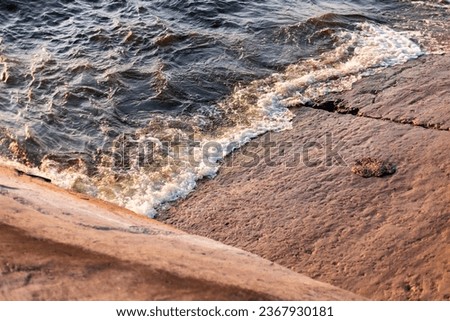 Blue stormy waves with sea foam breaking on concrete slab, sea texture view directly above on sunset
