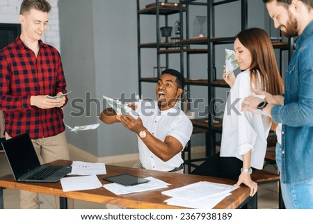 Happy business team of young multi-ethnic employees celebrating victory and big profit at office workplace. Cheerful excited young business man and woman throwing away banknote. Rain of money.