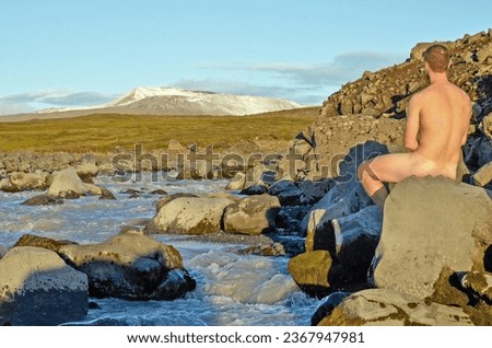 Young man enjoys nature while watching a glacier by a glacier creek in the idyllic landscape of the highlands of Iceland