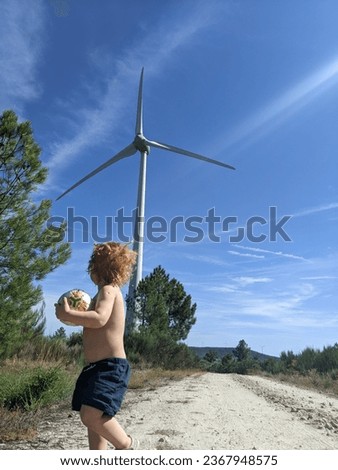 Young fascinated child admires the impressive size of a wind turbine from up close Royalty-Free Stock Photo #2367948575
