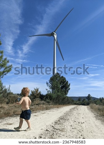 Young fascinated child admires the impressive size of a wind turbine from up close Royalty-Free Stock Photo #2367948583