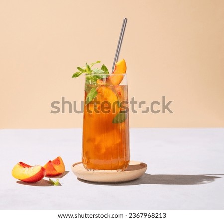 Refreshing peach ice and mint tea. Vegan homemade cold summer drink on tall glass on a light background with fresh fruits and shadows. Front view and free space for text. Royalty-Free Stock Photo #2367968213