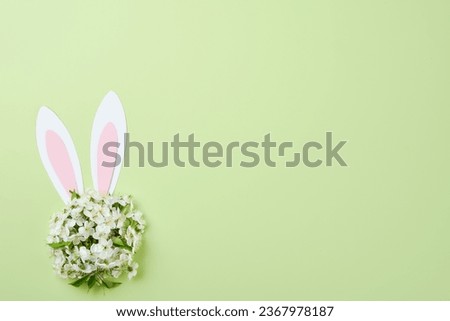 Happy Easter. Bunny rabbit ears made of pink paper and round bouquet of springs fresh cherry or apple blossoms on green background. Easter greeting card with copy space. Happy Easter concept. Mock up