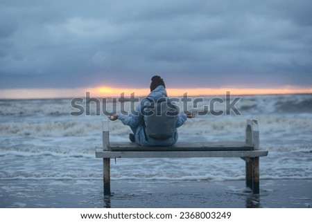 Lonely girl sitting on a bench by the sea in a winter storm. High quality photo.