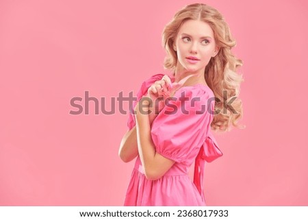 Feminine beauty. Portrait of a cute blonde girl with delicate pink makeup posing in an elegant pink dress on a pink studio background. Copy space. Hairstyles, Hollywood wave.