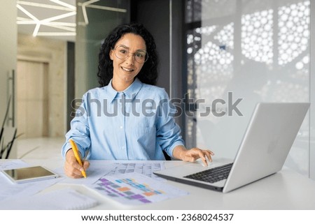 Portrait of young beautiful and successful financial accountant at workplace inside office, business woman smiling and looking at camera, writing documents and filling tables, inside office.