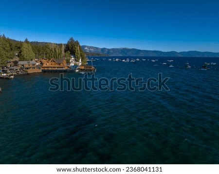 Aerial view of Lake Tahoe with blue water, surrounding mountains, boats, and nearby structures.