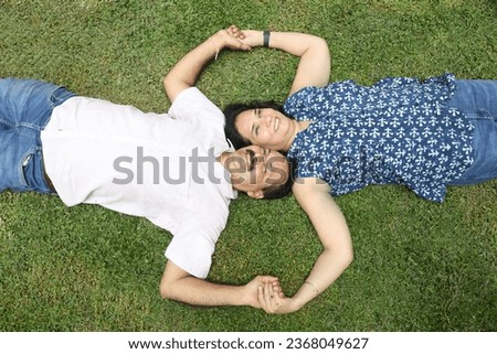 Indian happy couple lying down 
at park.