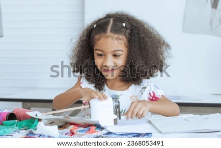 Cute African little girl sharpening pencil for sketching clothing design on paper at tailor room, cozy home as her dream, smiling with happiness, fun. Leisure, Lifestyle, Education, Kid Concept
