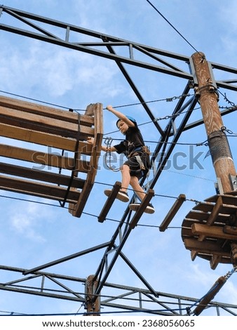 A teenage Caucasian boy in a rope amusement park crosses a suspension bridge. View from below