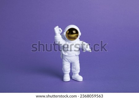 an astronaut figurine in a spacesuit exploring a plain purple background. Minimal creative still life colourful photography Royalty-Free Stock Photo #2368059563