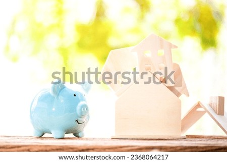 Piggy bank and the wooden home model put on the wood on nature bokeh in the public park, Loan or save money for buy a house and real estate concept