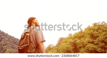 Traveler in the mountains, hiking. A man in a cap and with a backpack against the background of mountains looks into the distance on an autumn day