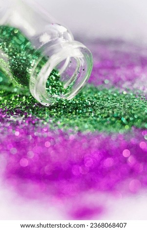Macro shot of a bottle with green and pink glitter spilled on a white background. Glitter banned from sale in Europe concept.