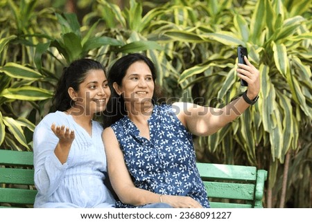 Mother and daughter taking selfie picture while sitting at park.