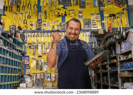 Handsome adult entrepreneur man in apron, with an expression of pride and happiness in her business full of hardware products. Royalty-Free Stock Photo #2368098889