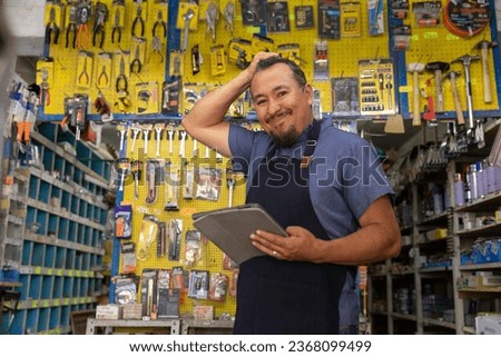 Handsome adult entrepreneur man in apron, with an expression of anger and frustration in her business full of hardware products. Royalty-Free Stock Photo #2368099499