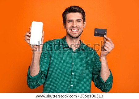 Photo of young promoter man wear green shirt hold debit card payment smartphone screen finance app isolated on orange color background