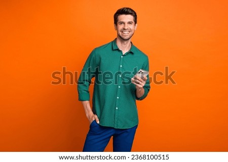 Photo of cheerful young man brunet hair hold new apple iphone gadget chatting broker working online isolated on orange color background