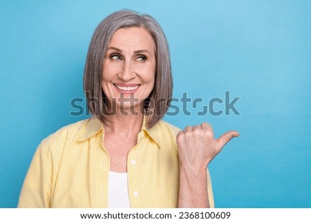 Photo of tricky dreamy woman dressed yellow shirt showing thumb looking empty space isolated blue color background