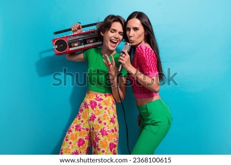 Photo of positive funky girls dressed colorful outfits singing mic listening boom box songs isolated blue color background