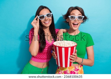 Photo of cute excited girls dressed colorful outfits watching movie enjoying pop corn isolated blue color background