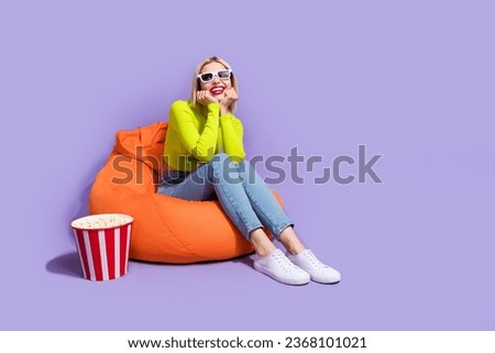 Photo of positive adorable girl wear trendy clothes sitting soft pouf enjoying free time empty space isolated on purple color background