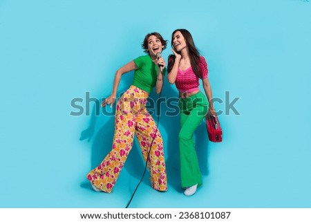 Full body photo of carefree two girlfriends optimistic singing hobby weekends take boombox solo song mike isolated on blue color background