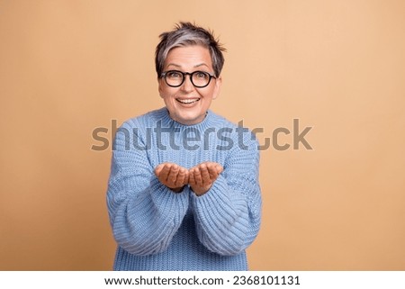 Photo portrait of cute grandmother palms hold empty space excited dressed stylish blue knitted garment isolated on beige color background