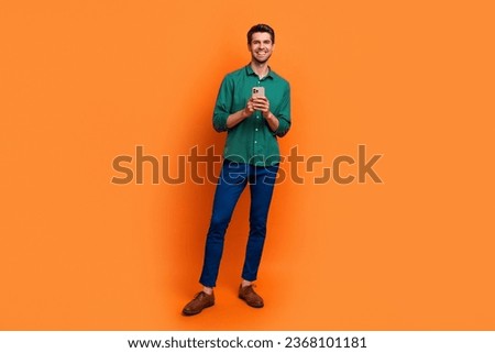 Full length photo of confident cute man dressed green shirt texting apple samsung iphone device isolated orange color background